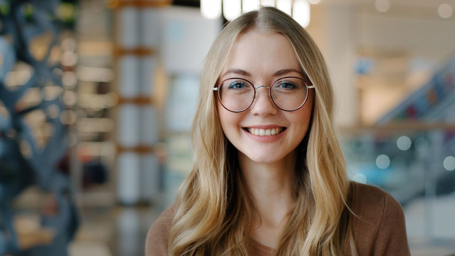 A young woman with glasses smiling in a library.