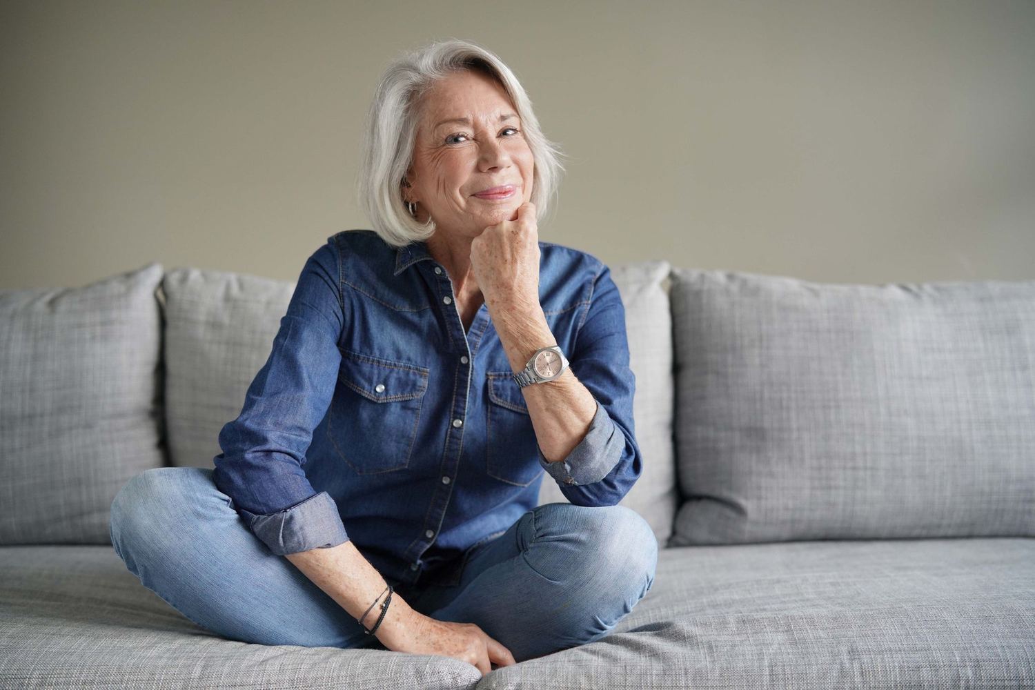 A woman in her fifties sitting on a sofa at home, thinking.