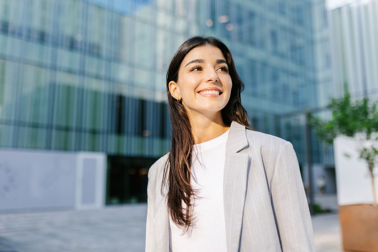 A woman in a suit walking past a tall glass office tower.