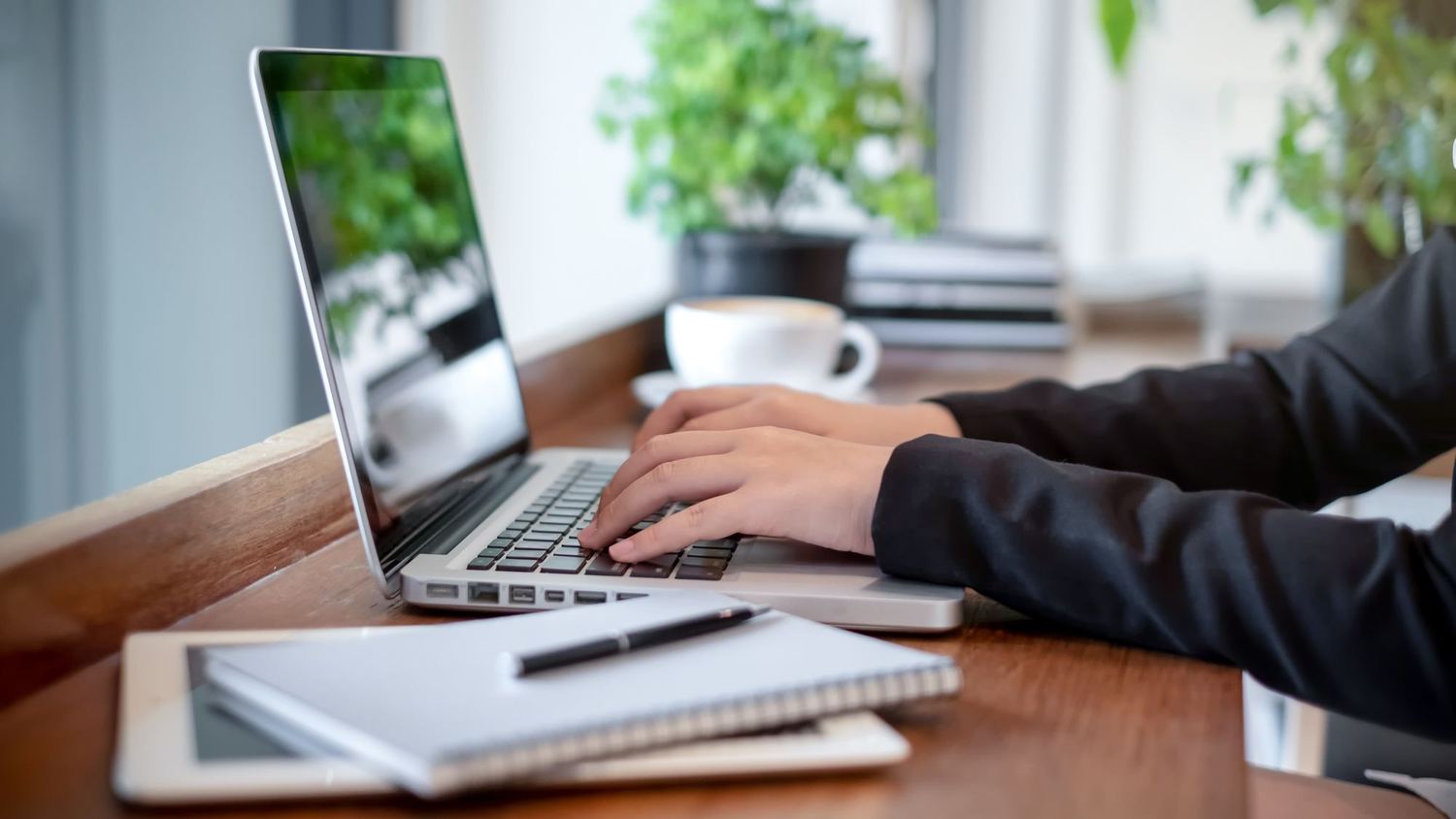 Hands typing on a laptop at a desk with a cup of coffee.