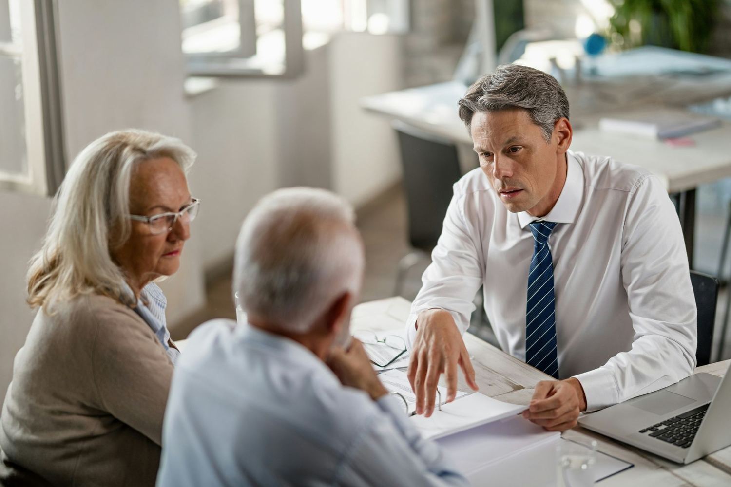 An older couple reviewing documents with an adviser at a desk.