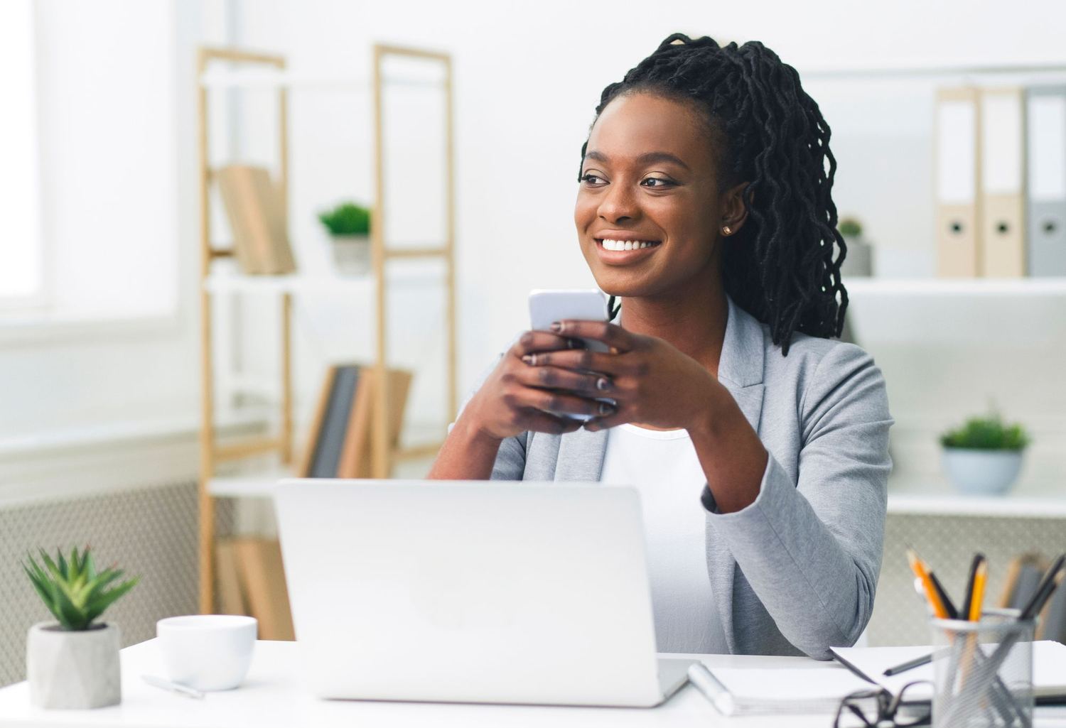 A woman at a desk holding a phone beside an open laptop.