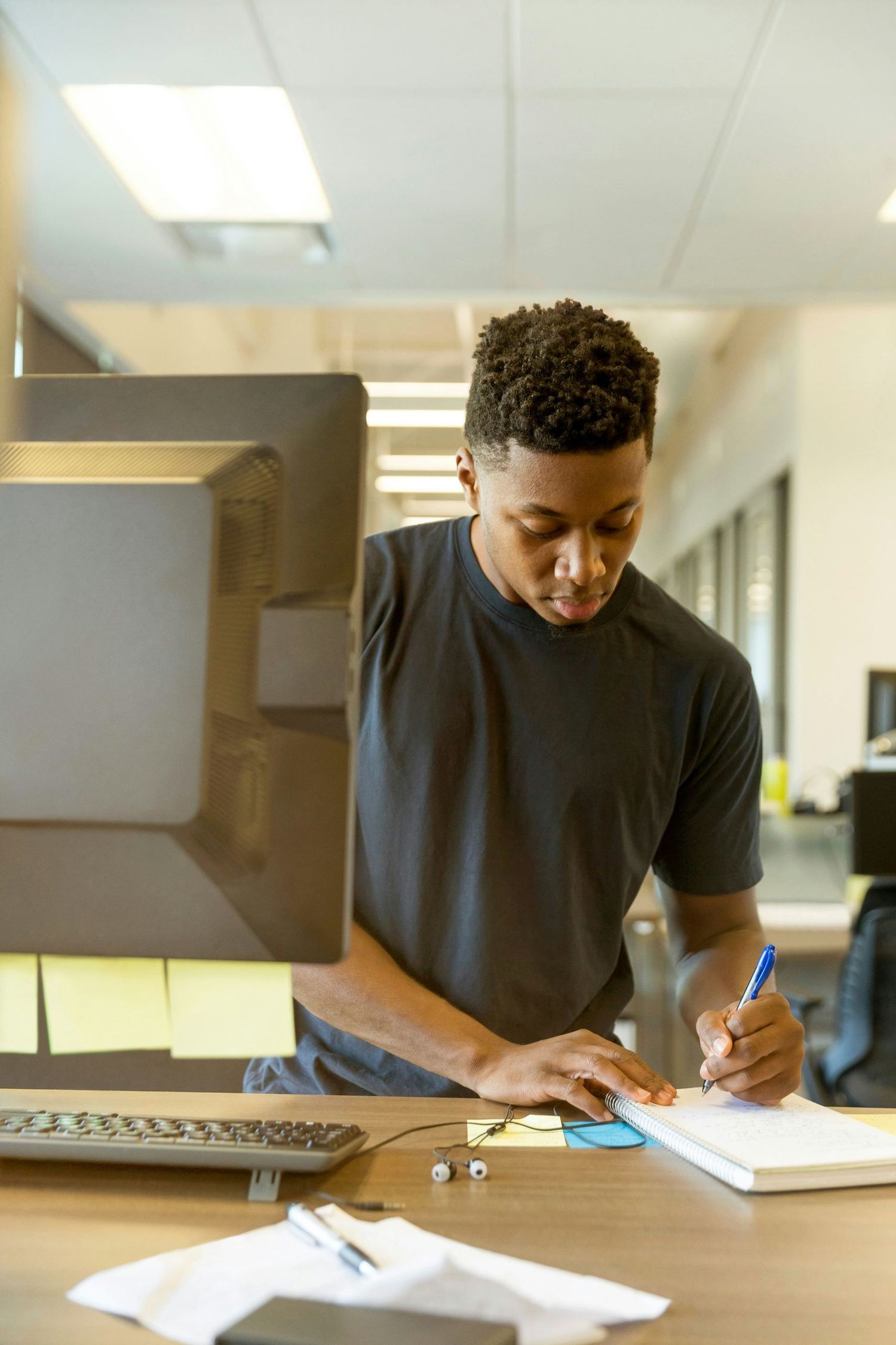 A young man writing at a desk in an office.
