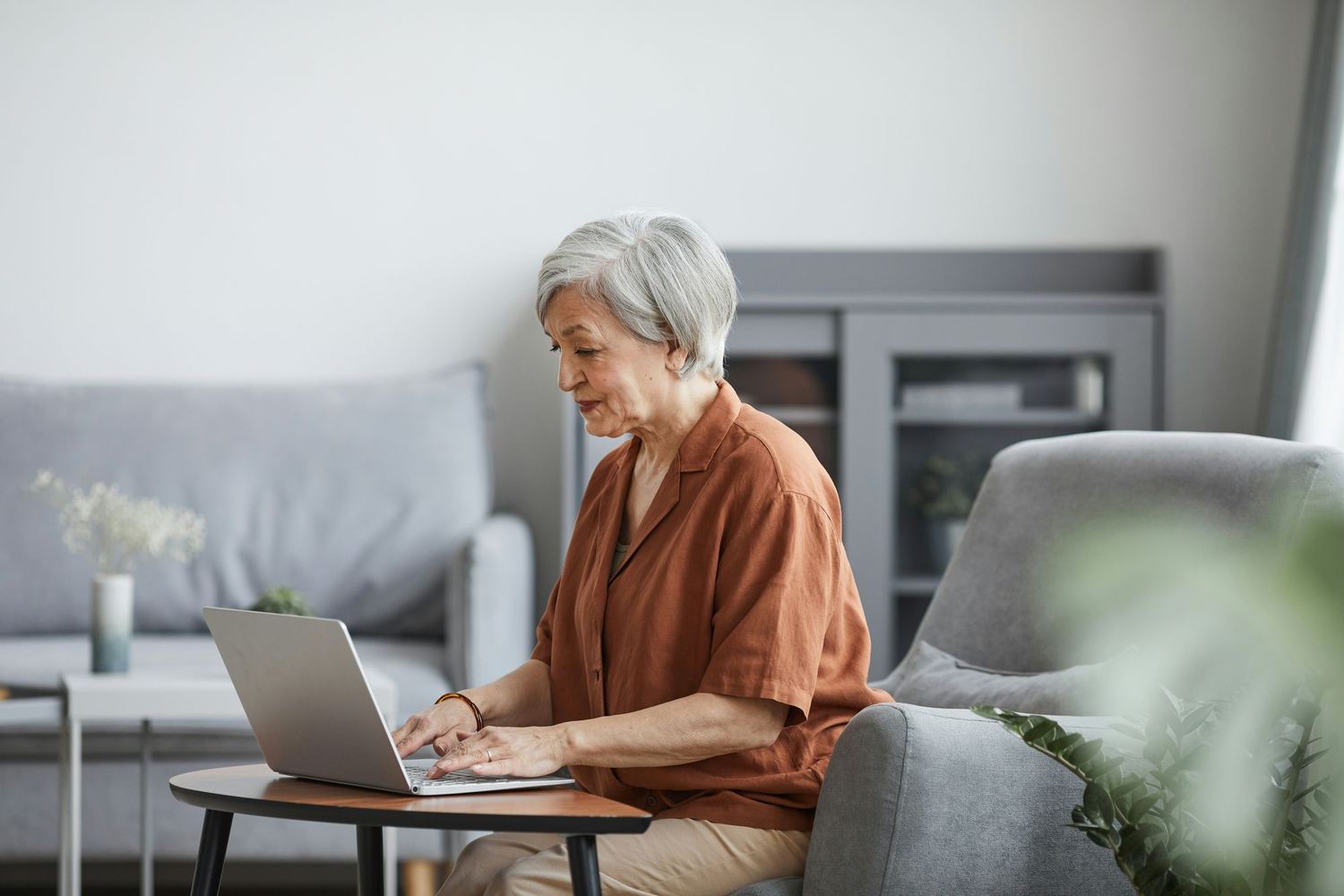 An older woman using a laptop at a side table at home.