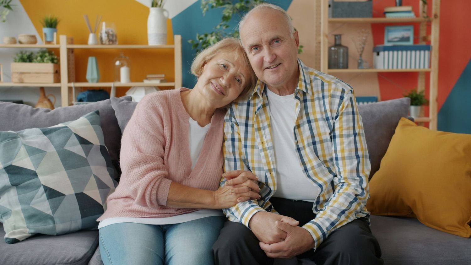 An older couple sitting close together on a sofa at home.