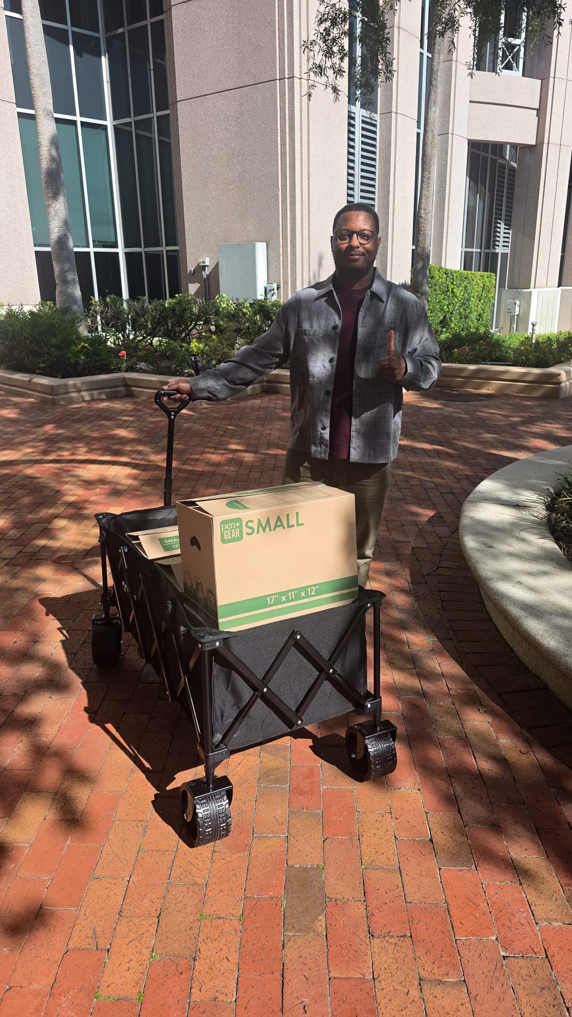 Derrick Johnson pulling a wagon of school supplies across a brick courtyard, giving a thumbs-up