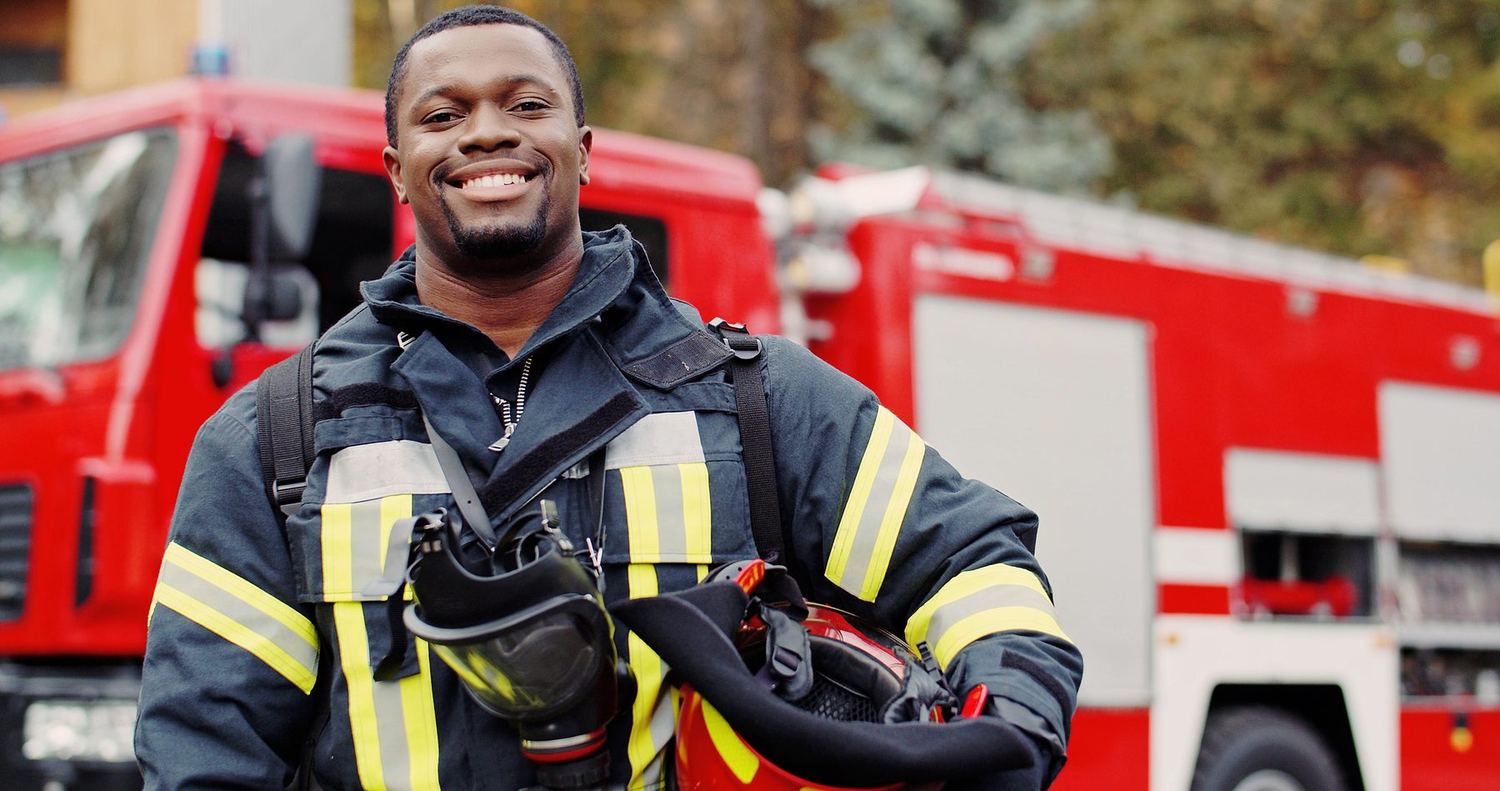 A firefighter in turnout gear smiling beside a fire engine